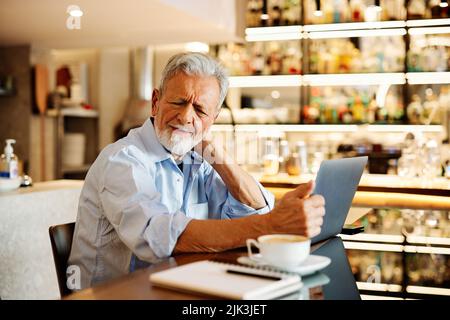 A senior student is sitting at home and rubbing his neck. He is tired of sitting and studying. Stock Photo