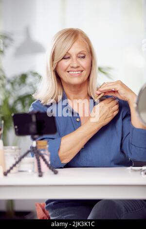 A happy blond senior woman is sitting at home and combing her hair. Daily routine Stock Photo