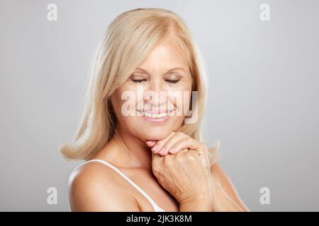 Smiling senior woman with eyes shut posing in studio. Stock Photo