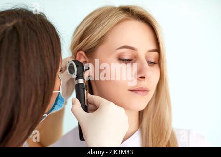 Otolaryngologist doctor examining patients ear with otoscope in clinic. Diagnosis of otitis media concept Stock Photo