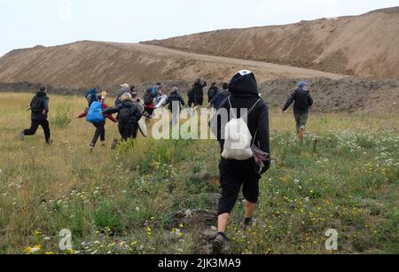 Schkeuditz, Germany. 30th July, 2022. Climate activists walk up the hill of a construction site of the logistics company DHL at Leipzig-Halle Airport. The action is to protest against the planned expansion of the air cargo hub. Credit: Sebastian Willnow/dpa/Alamy Live News Stock Photo