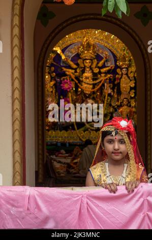 Howrah,India -October 26th,2020 : Bengali girl child in festive dress, smiling and posing with Goddess Durga in background, inside decorated home. Stock Photo