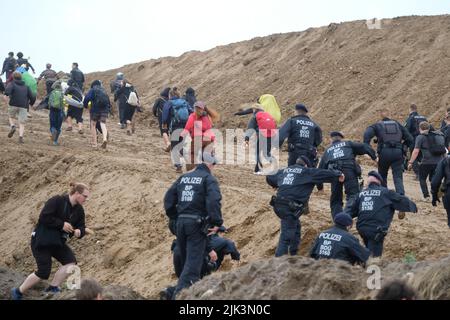 Schkeuditz, Germany. 30th July, 2022. Climate activists and police officers walk up the hill of a construction site of the logistics company DHL at Leipzig-Halle Airport. The action is to protest against the planned expansion of the air cargo hub. Credit: Sebastian Willnow/dpa/Alamy Live News Stock Photo