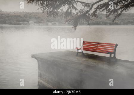 A red park bench at the lake in the fog, concept of grief and loss Stock Photo