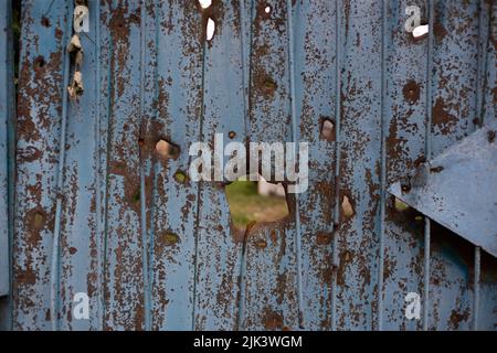 Fence near the house with bullet holes and charapnels after gunshots and fighting during the invasion of Russian troops into Ukraine Stock Photo