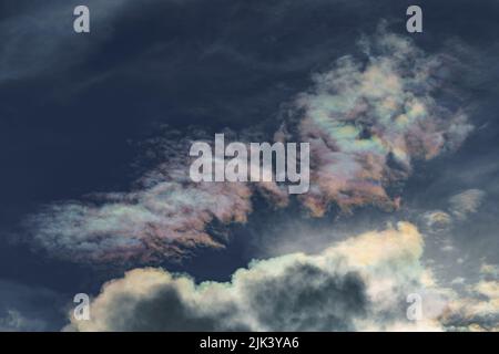 Diffraction of light on drops of supercooled water in clouds, rainbow clouds against the blue sky in clear sunny weather, irisation of cumulus clouds Stock Photo