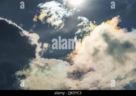 Diffraction of light on drops of supercooled water in clouds, rainbow clouds against the blue sky in clear sunny weather, irisation of cumulus clouds Stock Photo