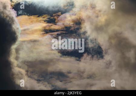 Diffraction of light on drops of supercooled water in clouds, rainbow clouds against the blue sky in clear sunny weather, irisation of cumulus clouds Stock Photo