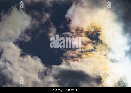 Diffraction of light on drops of supercooled water in clouds, rainbow clouds against the blue sky in clear sunny weather, irisation of cumulus clouds Stock Photo