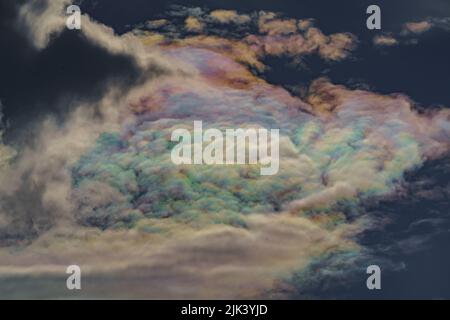 Diffraction of light on drops of supercooled water in clouds, rainbow clouds against the blue sky in clear sunny weather, irisation of cumulus clouds Stock Photo