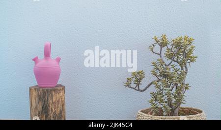 Costumbrista scene with a pink jug on a wooden trunk and a pot with plantain and green leaves. Textured bluish wall background Stock Photo