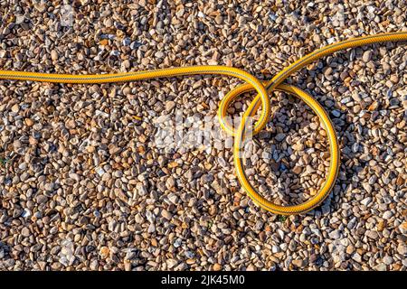 Coils of a garden hosepipe on a gravel drive. Stock Photo