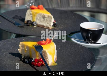 Delicious fresh cheesecakes decorated with berries and a cup of coffee on a table in a street restaurant Stock Photo