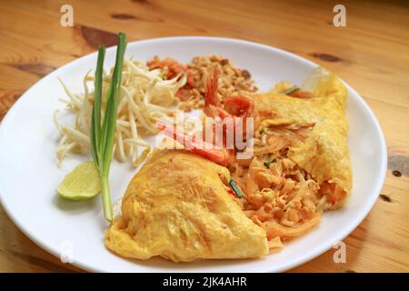 Plate of Pad Thai, Flavorful Thai Style Fried Noodle Wrapped in Fried Egg and Topped with Prawns Stock Photo