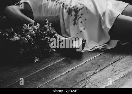 A girl in a bloody white dress lies on the floor of the house and next to a bouquet of flowers, the war in Ukraine, a girl killed by a Russian soldier Stock Photo