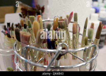 Artist paintbrushes stand ready for use with other art supplies in a still life. Stock Photo