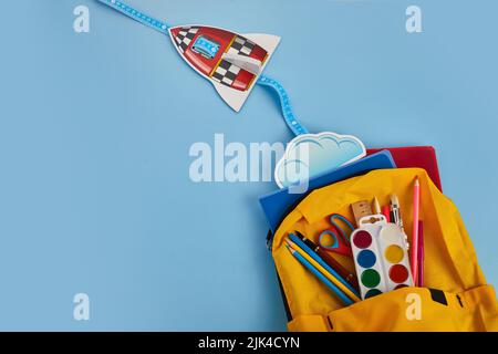 School backpack with colorful school supplies and rocket on blue background Stock Photo
