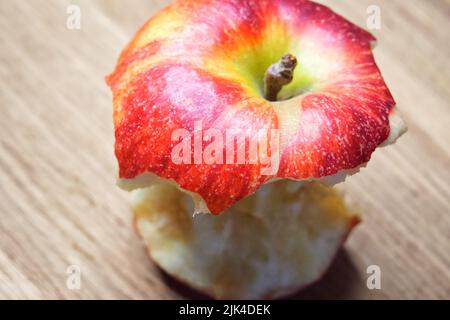 Red apple core on a wooden background. A bitten apple close-up. Stock Photo