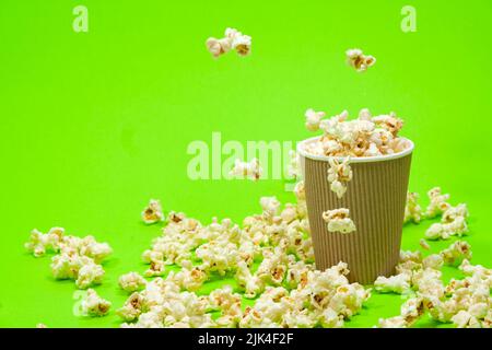 Popcorn is poured into a paper brown glass on a green background with place for text Stock Photo