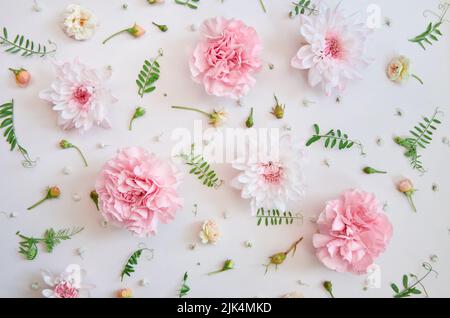 Pink flowers and green leaves on white floral pastel background. Flat lay Stock Photo