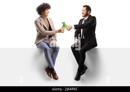 Colleagues sitting on a blank panel and toasting with bottles of beer isolated on white background Stock Photo