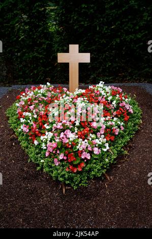 colorful heart shaped flower arrangement on a grave with wooden cross Stock Photo