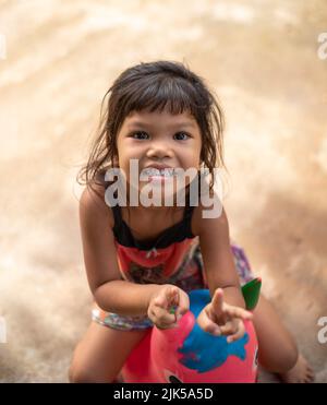 A young Thai girl smiles at the camera while sitting on a space hopper toy Stock Photo