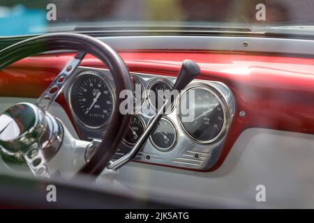Steering wheel on a custom 1950's Ford F100 pick up truck with stainless steel control panel, dials and red metal coachwork in the background Stock Photo