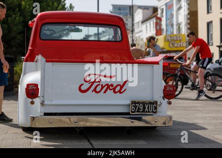 A Ford F100 1950's custom pick up truck in red and white. Rear view. parked on a street with pedestrians looking. Stock Photo