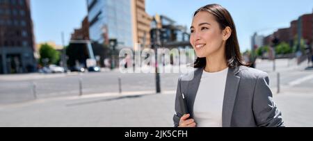 Young smiling proud Asian business woman entrepreneur standing on city street. Stock Photo