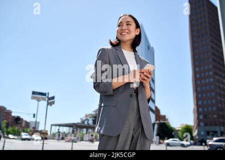 Young successful Asian business woman using phone standing on city street. Stock Photo