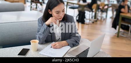 Young serious Asian business woman using laptop working in modern office. Stock Photo