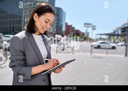 Young happy Asian business woman executive using digital tablet on city street. Stock Photo