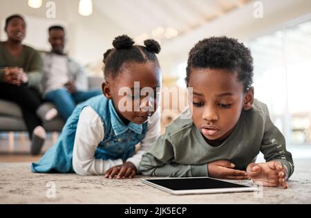 Say goodbye to bored kids with entertaining ebooks. an adorable little boy and girl using a digital tablet with their family in the background at home Stock Photo