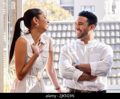 Your jokes are always the funniest. two cheerful young businesspeople standing at a window in an office. Stock Photo