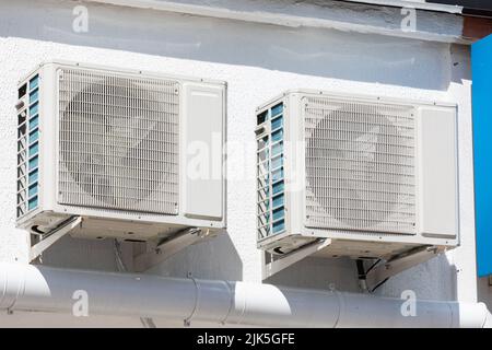 two units of outdoor air conditioners for heat dissipation are hung on the wall outside the building Stock Photo