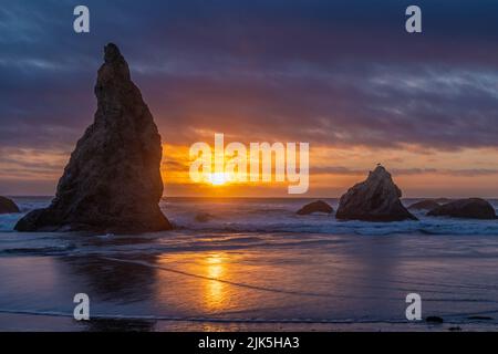 Sun and sky reflected on Bandon Beach at sunset with sea stacks in silhouette on the Pacific Coast in Bandon, Oregon. Stock Photo
