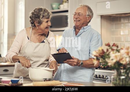 This is going to be so much fun. a senior couple using a digital tablet while baking at home. Stock Photo