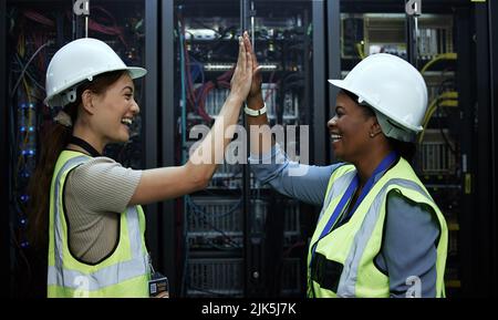 We did it. two attractive female programmers high fiving in a server room. Stock Photo
