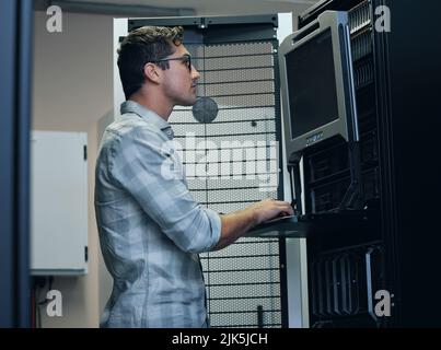 Checking out the code. a handsome young male programmer working on a computer in a server room. Stock Photo