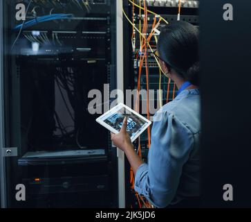 I see what the issue is. Rearview shot of an unrecognizable female programmer working on a tablet in a server room. Stock Photo
