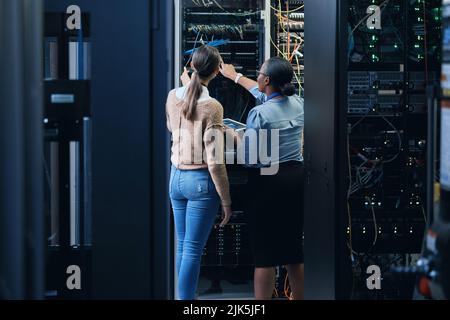 Theyre on the case. Rearview shot of two unrecognizable female programmers working together in a server room. Stock Photo