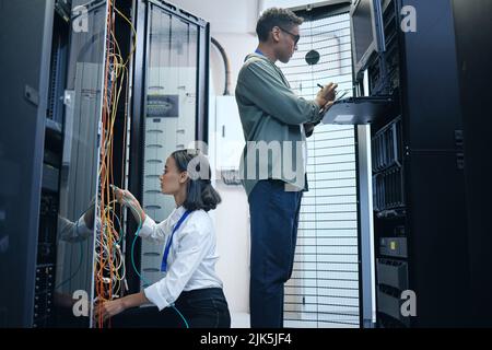 They make a great team. two young computer programmers working together in a server room. Stock Photo