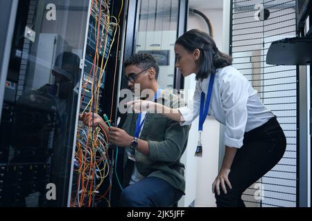 An extra set of eyes always helps. two young computer programmers working together in a server room. Stock Photo