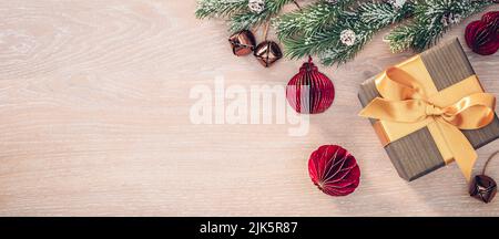Christmas gift with golden ribbon bow, Christmas tree branch and decorations on light oak wood background Stock Photo