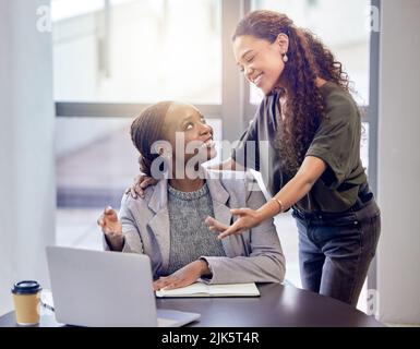 Can you take a look at this. two young female colleagues talking while using a laptop in an office at work. Stock Photo