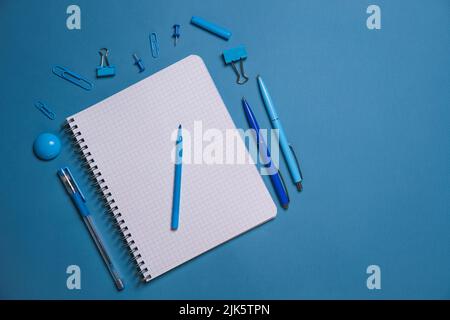 Stationery. Open notebook pencils and pens, stickers and binding clips. Copy space and notes. Writing tools. Office tools. Isolated on blue background Stock Photo