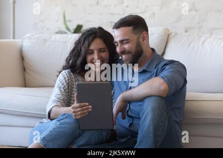 Cheerful couple of satisfied gadget users sitting on floor Stock Photo