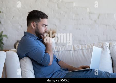 Serious pensive millennial freelance business man resting on sofa Stock Photo