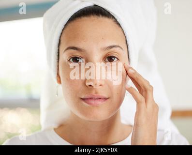 If you have a good moisturiser then you have everything you need. a beautiful young woman applying moisturiser to her face. Stock Photo